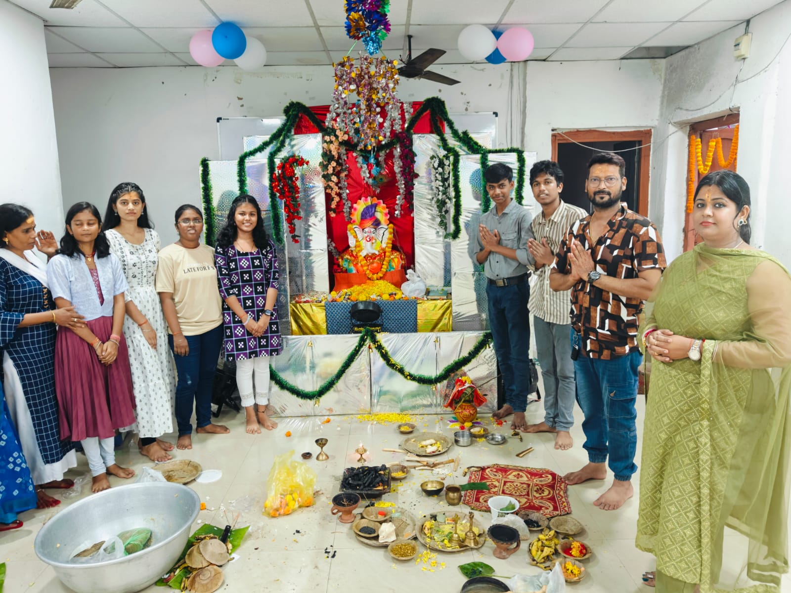 Students and teachers in namaste posture celebrating Ganesh Puja in front of idol